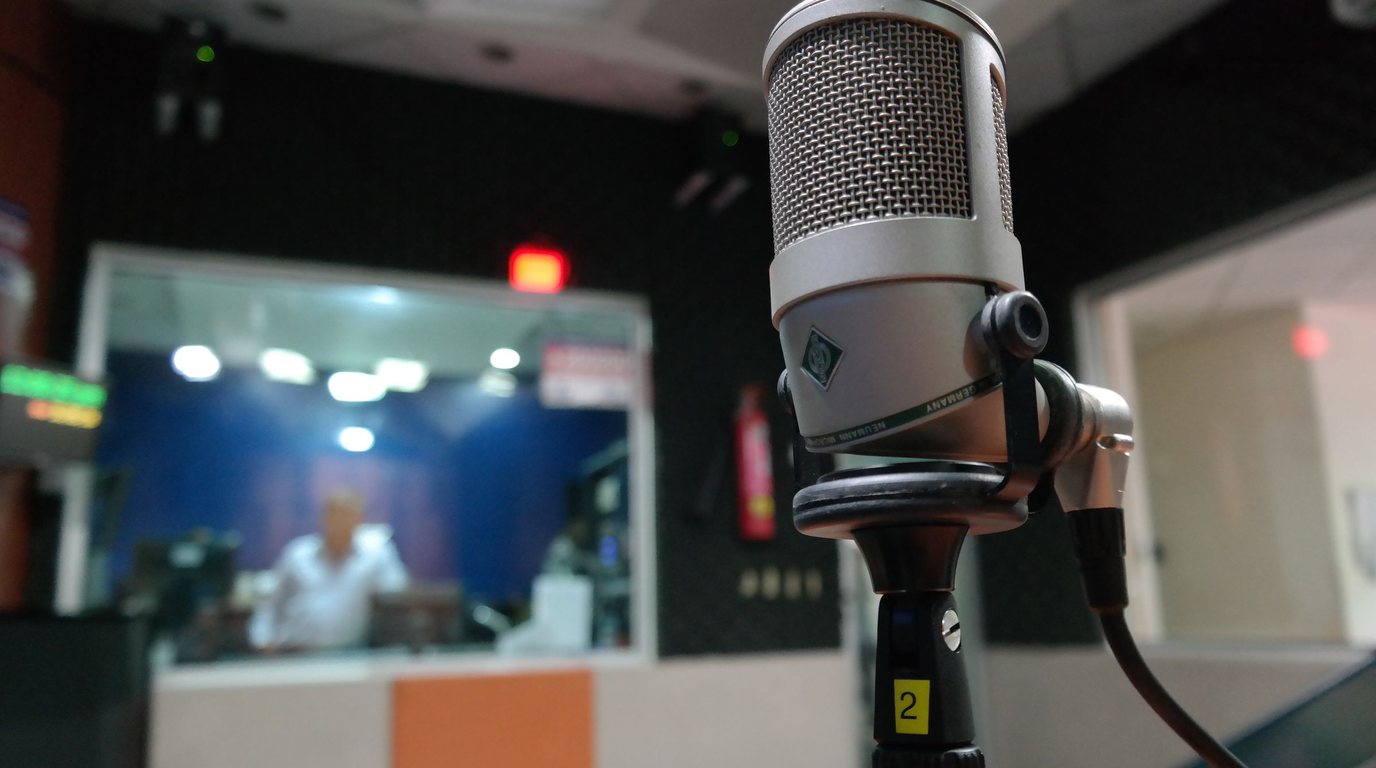 Stock photo: a studio microphone with a speaker recording in the booth behind