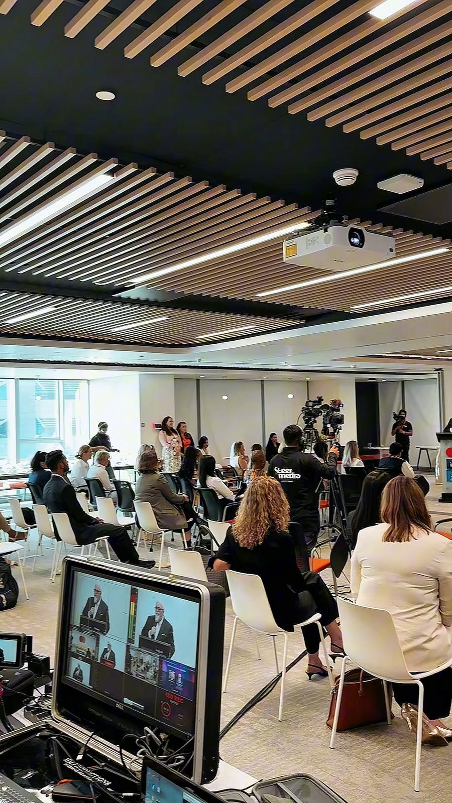 A conference room with a live monitor in the foreground, behind the scenes at an event