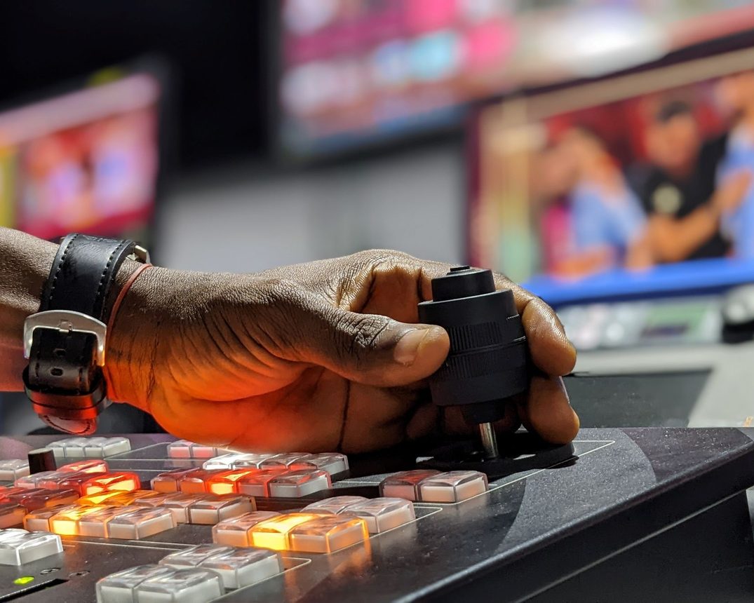Stock photo: an operator's hand on a video switcher, with live monitors in the background